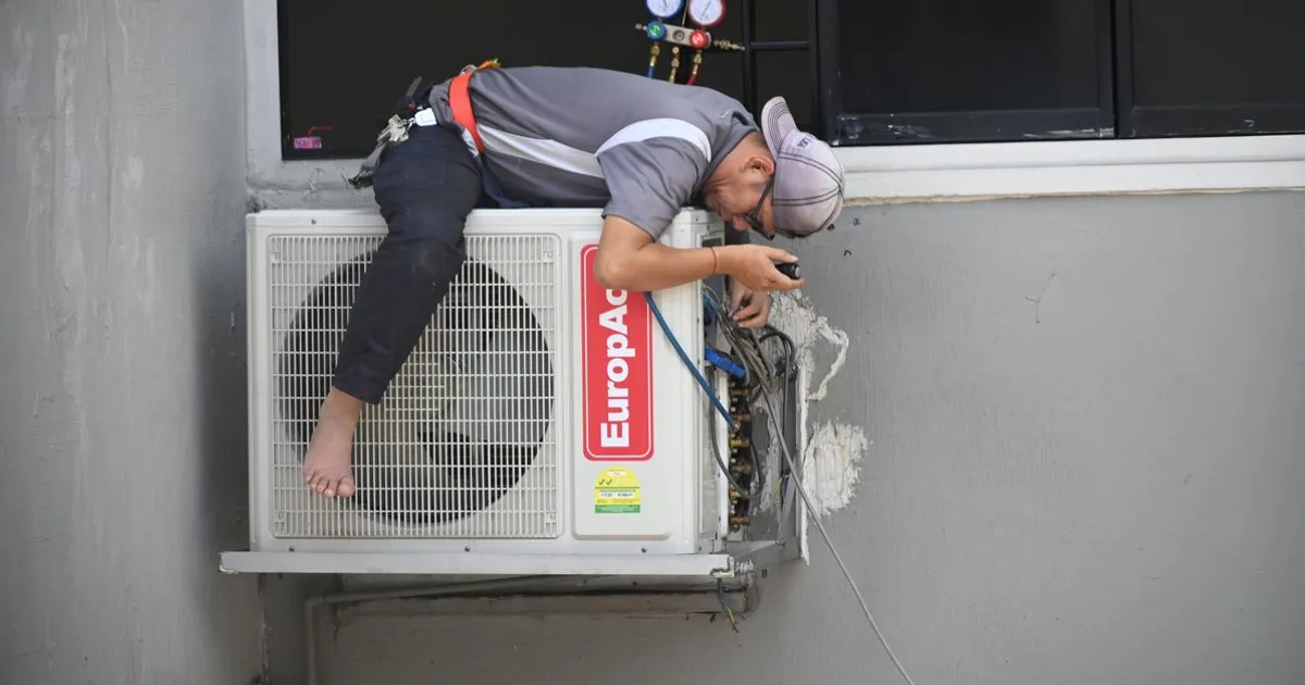 HVAC technician servicing an outdoor air conditioning condenser with tools