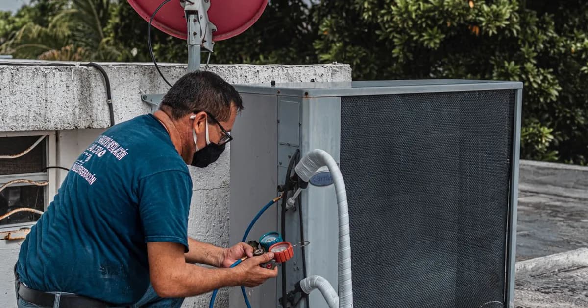 HVAC technician using manifold gauges on an outdoor air conditioner while studying refrigerants