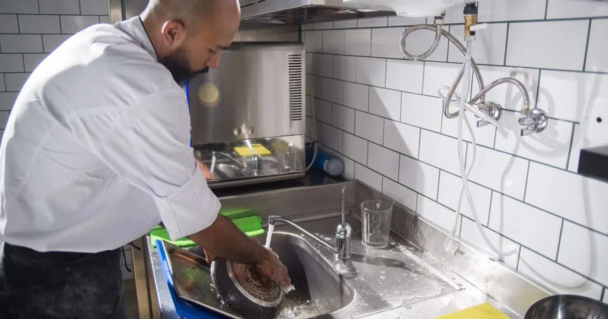 Chef washing utensils at a stainless-steel commercial kitchen sink